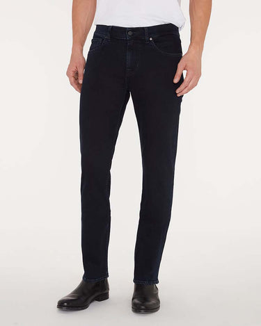 A person wearing7 For All Mankind Slimmy Jeans, Blue Black with a white t-shirt and black leather boots, shown from the waist down against a plain white studio background.