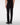 Rear view of a person wearing 7 For All Mankind Slimmy Jeans in Black and black leather shoes against a plain light gray studio background.
