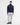 A man modeling a Barbour Tisbury Half Zip Jumper in Navy sweater, paired with off-white trousers, a white shirt, and dark leather shoes, against a plain white studio background.