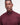 A close-up shot of a man wearing Barbour Tisbury Half Zip Jumper in Ruby sweater with a distinctive silver metal O-ring zipper pull, set against a plain light gray background.