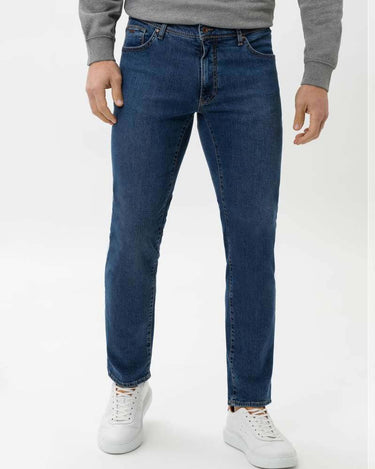 A person wearing Brax Cadiz Straight Fit Jeans, Blue Used, a gray long-sleeve top, and white sneakers, shown from the waist down against a plain white studio background.