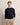 A man wearing a Bugatti Organic Cotton Crew Neck, Navy over a white undershirt and beige trousers, standing against a plain beige studio background.