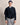 Man wearing a Bugatti V Neck Jumper, Navywith a belt, striped shirt, and gray pants on a beige background