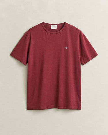 A GANT Shield T-Shirt in Deep Grape in a washed, muted burgundy red, featuring a small embroidered shield logo on the left chest, laid flat against a light beige background.