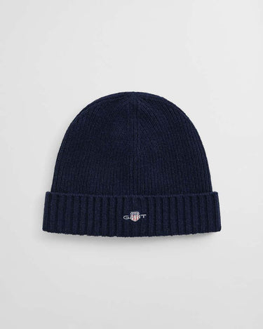 A GANT Shield Wool Beanie in Navy with a small embroidered GANT shield logo on the front of the folded cuff, shown against a light gray background.