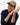 A smiling man wearing a Tommy Hilfiger 1985 Brushed Baseball Cap, Camel with a small embroidered logo, a navy blue knit sweater, and a brown leather strap watch, posed against a plain white background.
