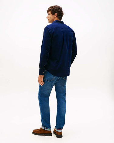 A man wearing a Tommy Hilfiger Fine Corduroy Shirt in Navy, blue jeans, and brown suede boots, shown from a rear three-quarter view against a plain white studio background.