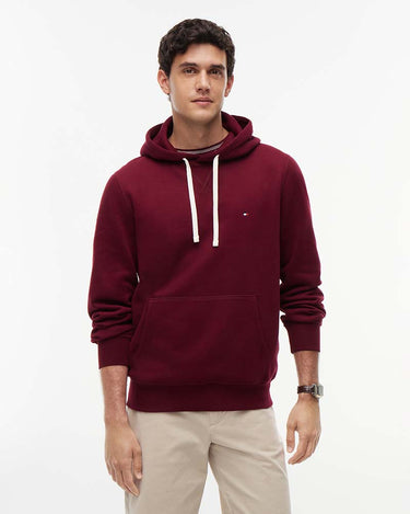 A man wearing a Tommy Hilfiger Peached Fleece Hoodie, Winewith white drawstrings and a small embroidered logo on the chest, paired with beige trousers, against a plain white studio background.