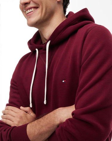 A man wearing a Tommy Hilfiger Peached Fleece Hoodie, Wine with white drawstrings and a small Tommy Hilfiger flag logo on the chest, shown against a plain white background.