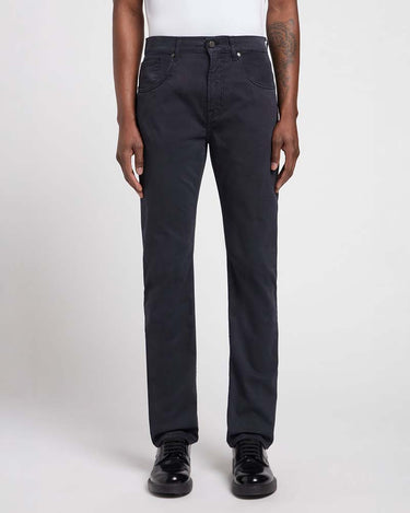 A person wearing 7 For All Mankind Sateen Trousers, Navy, a white top, and black leather shoes, standing against a light gray studio background.