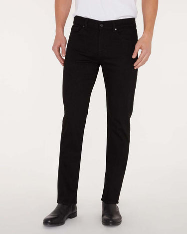A person 7 For All Mankind Slimmy Jeans, Black with a white shirt and black leather boots, shown from the waist down against a plain light background.