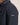 Close-up of a person wearing a Bugatti All-Season Jacket, Navy, showing the shoulder, collar, and a small rectangular Gucci logo patch on the upper sleeve against a plain light beige background.
