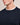 Close-up of a man wearing a Bugatti Organic Cotton Crew Neck, Navysweater with a white ribbed inner collar and a small tonal embroidered logo on the chest, set against a plain beige background.