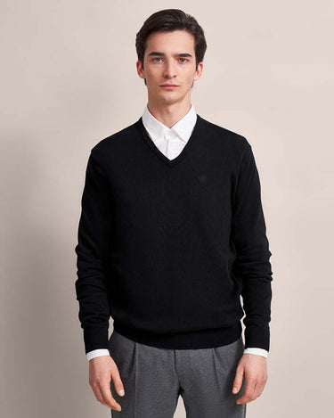 Man wearing a Bugatti V Neck Jumper, Black over a white shirt with gray pants on a beige background