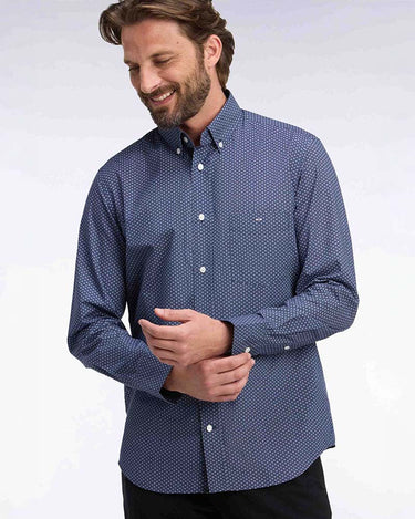A man wearing a blue and white micro-patterned long-sleeve button-down shirt, shown from the waist up against a light gray studio background.