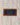 Close-up of a brown leather patch label with a blue center reading 'The Velo-Speed Jacket' and 'A TRUE HACKETT ICON' on a cream plaid fabric background.