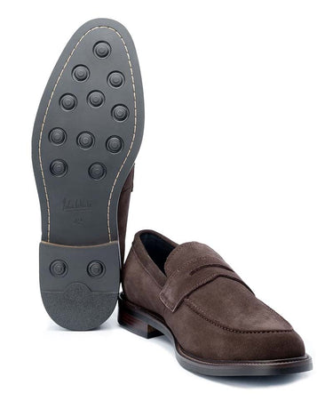A pair of John White Banff Suede Penny Loafers, Brown, with one shoe standing upright to show the textured black rubber outsole and the other lying flat to show the side profile and toe.