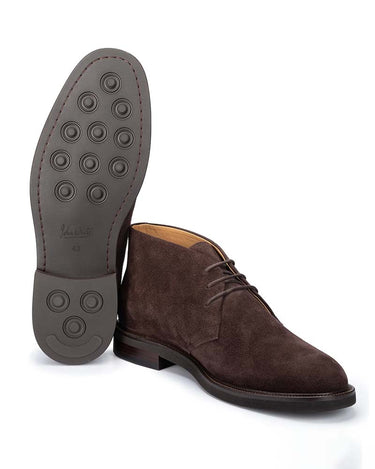 A pair of John White Wessex Suede Chukka Boots, Brown, with one boot standing upright to show the textured gray outsole and the other lying on its side to show the profile and toe.