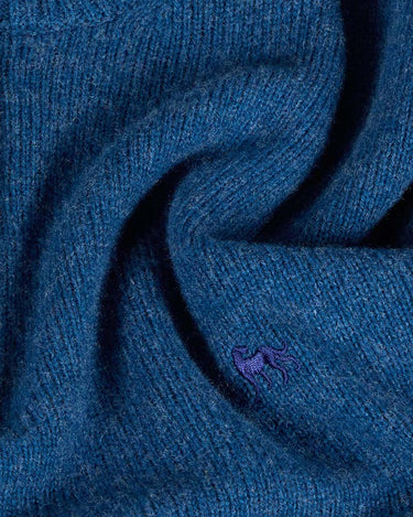 A close-up of a textured blue knit fabric with a small purple embroidered lobster logo, indicating the Lacoste brand.