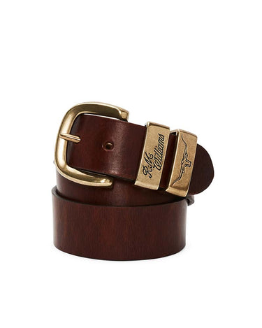 A R.M. Williams Drover Belt, Mid Brownwith a polished gold-tone buckle and matching decorative metal keeper, coiled on a white background. The keeper features the script brand name 'Ralph Lauren'.