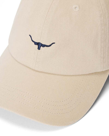 A close-up of a R.M. Williams Longhorn Twill Cap, Ecru featuring a navy blue embroidered longhorn logo on the front panel, set against a clean white background.