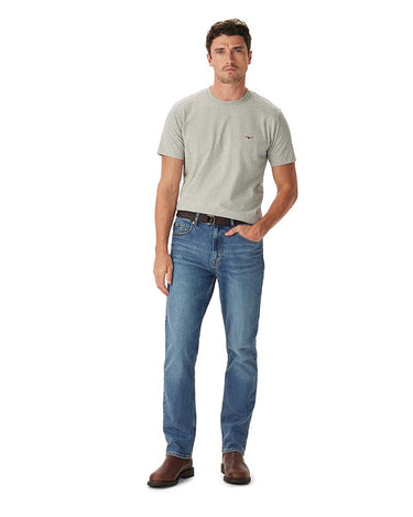 A man modeling a R.M. Williams Parson T-Shirt, Grey Marleand blue jeans with brown leather shoes, standing against a solid white background.