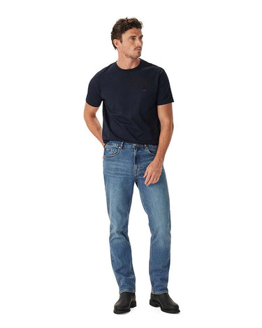 A man modeling a R.M. Williams Parson T-Shirt, Navy and blue jeans against a solid white background.