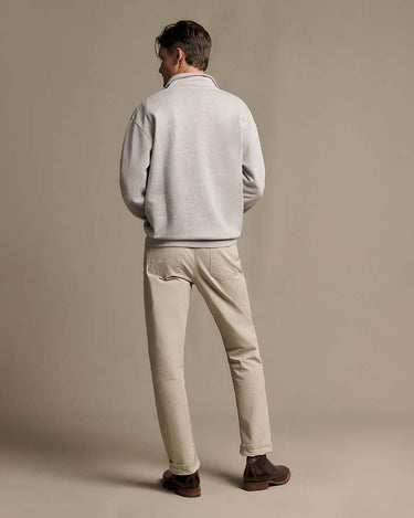 A man viewed from behind wearing a R.M. Williams Quarter Zip Sweat, Grey Marle, beige trousers, and brown boots, standing against a solid beige studio background.