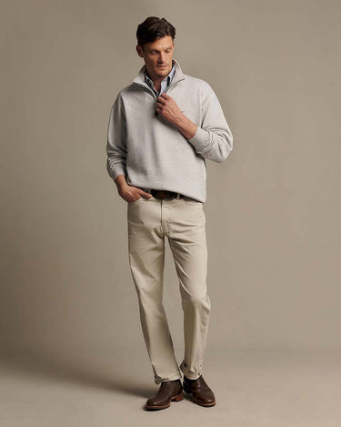 A man modeling a R.M. Williams Quarter Zip Sweat, Grey Marle, paired with beige trousers and brown leather shoes, against a solid warm gray studio background.