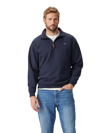 A man wearing a R.M. Williams Quarter Zip Sweat, Navy with a small embroidered logo on the left chest, paired with blue jeans and a white undershirt, standing against a solid white background.