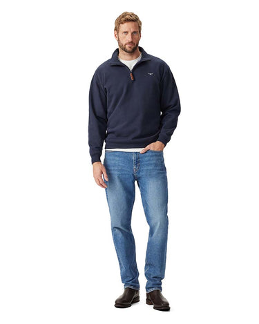 A man modeling a R.M. Williams Quarter Zip Sweat, Navy with a small white embroidered logo on the left chest, paired with blue jeans and dark brown boots, against a solid white background.