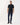 A man modeling a R.M. Williams Rod Pique Polo, Navywith dark blue jeans and black shoes, standing against a plain white studio background.