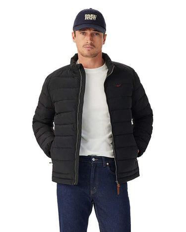 A man wearing a R.M. Williams Rydal Padded Jacket, Black, a white t-shirt, blue jeans, and a navy blue baseball cap with 'PUSH LOVEY' embroidered on the front, photographed against a solid white background.
