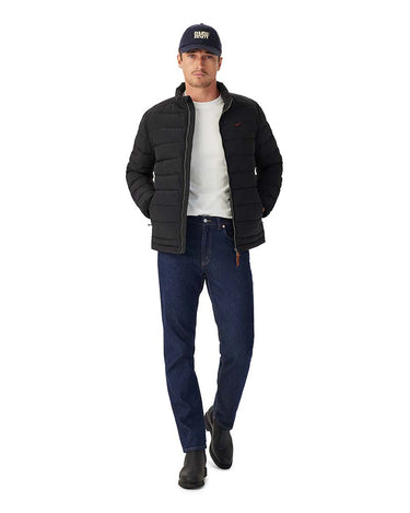 A man modeling a R.M. Williams Rydal Padded Jacket, Black, dark blue jeans, a white t-shirt, black boots, and a navy baseball cap with 'BON' embroidered on the front, set against a plain white background.