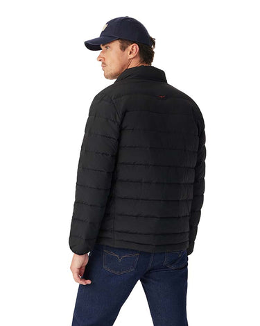 A man wearing a R.M. Williams Rydal Padded Jacket, Black, navy blue baseball cap, and dark blue jeans, shown from a side-back angle against a plain white background.