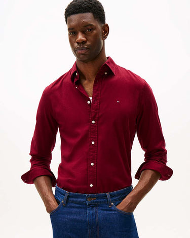 A man wearing a Tommy Hilfiger Flex Flannel Shirt, Burgundy with rolled-up cuffs and blue jeans, standing against a plain white studio background.