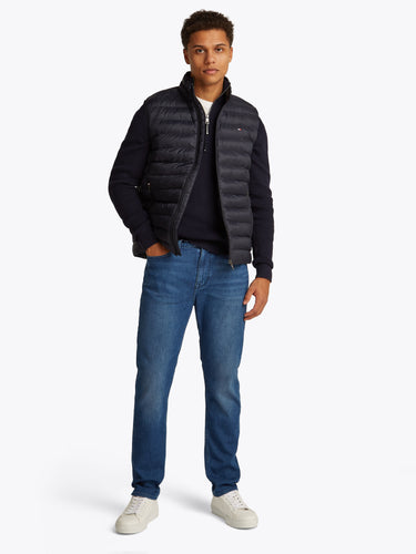 Man wearing a Tommy Hilfiger Packable Quilted Gilet, Navy, dark shirt, blue jeans, and white shoes on a white background