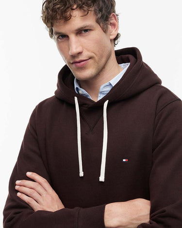 A man wearing a Tommy Hilfiger Peached Fleece Contrast Drawstring Hoodie with white drawstrings, layered over a light blue collared shirt, photographed against a clean white background.